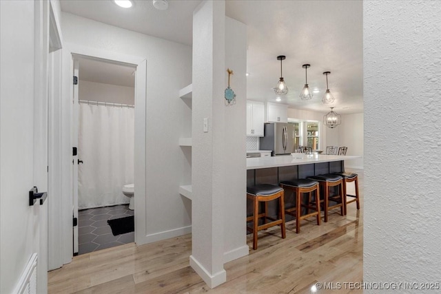 kitchen with a textured wall, freestanding refrigerator, a kitchen bar, light wood-style flooring, and white cabinetry