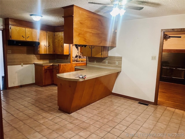 109 Ash Ave, Fort Gibson, OK 74434 - kitchen featuring a peninsula, ceiling fan, a textured ceiling, and brown cabinets