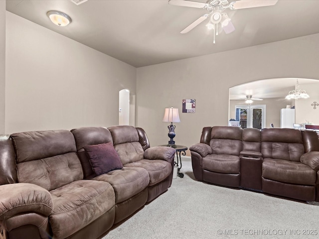 living area with arched walkways, ceiling fan with notable chandelier, and carpet flooring