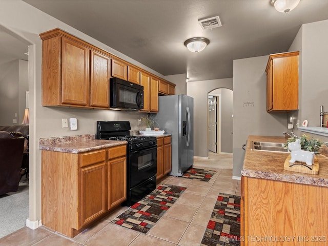 kitchen with a sink, light tile patterned floors, black appliances, visible vents, and arched walkways