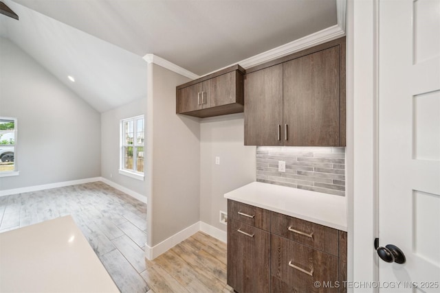 919 E 11th St, Claremore, OK 74017 - kitchen featuring backsplash, light countertops, light wood-type flooring, vaulted ceiling, and dark brown cabinetry
