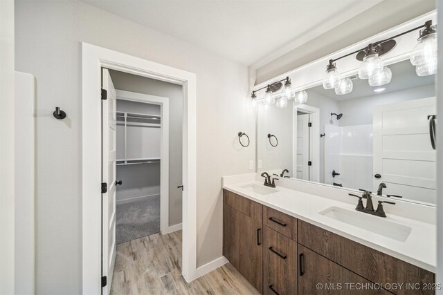919 E 11th St, Claremore, OK 74017 - full bathroom with a shower, double vanity, a walk in closet, wood finished floors, and baseboards