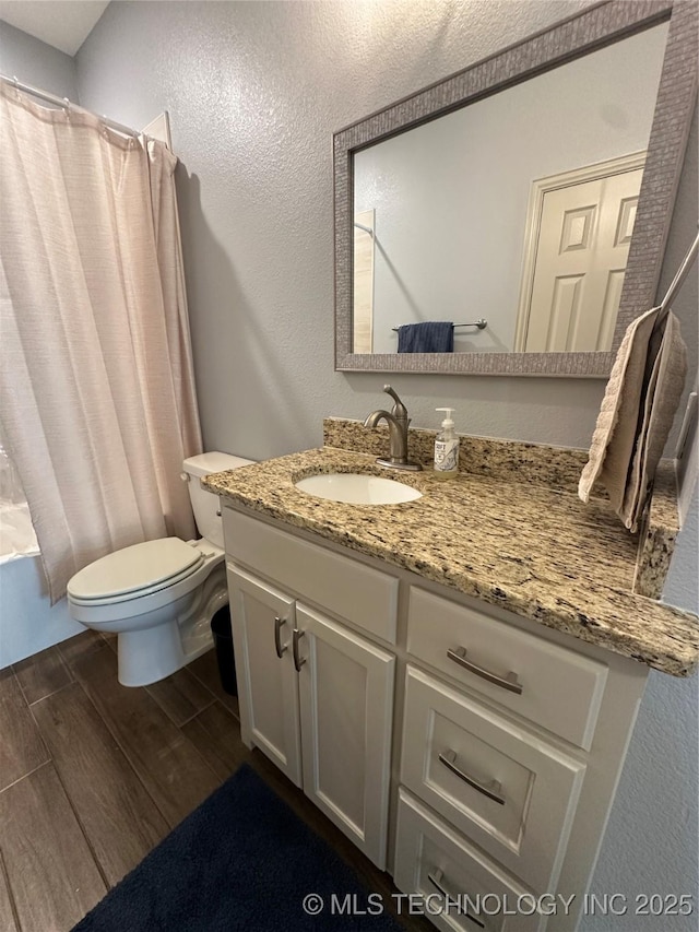full bathroom with shower / bath combo, wood finished floors, vanity, a textured wall, and toilet