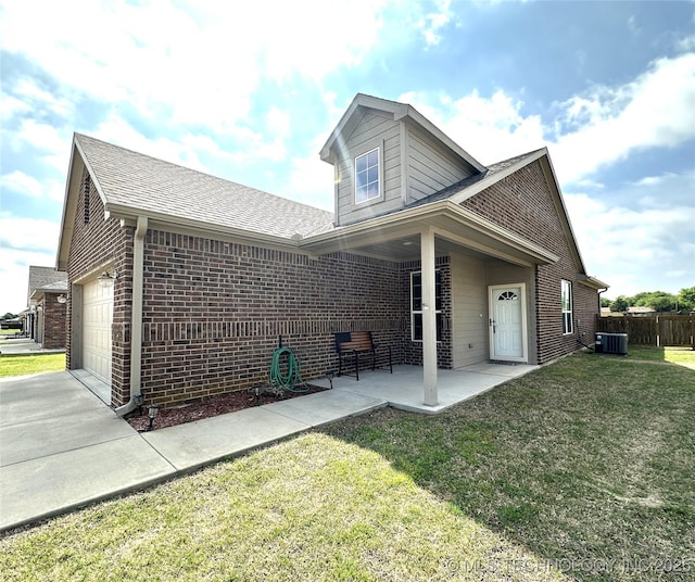 rear view of house with central AC unit, a lawn, concrete driveway, an attached garage, and brick siding