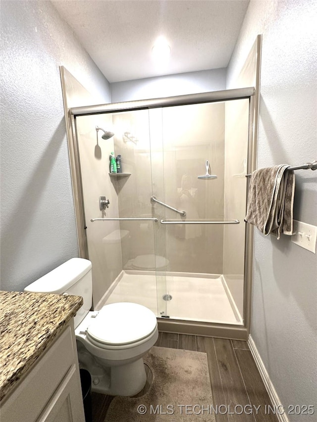 bathroom featuring wood finished floors, vanity, toilet, and a stall shower