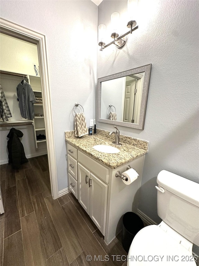 bathroom with baseboards, wood finished floors, toilet, and vanity