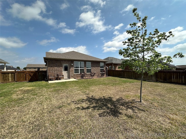 back of property with a fenced backyard, brick siding, a yard, and a patio