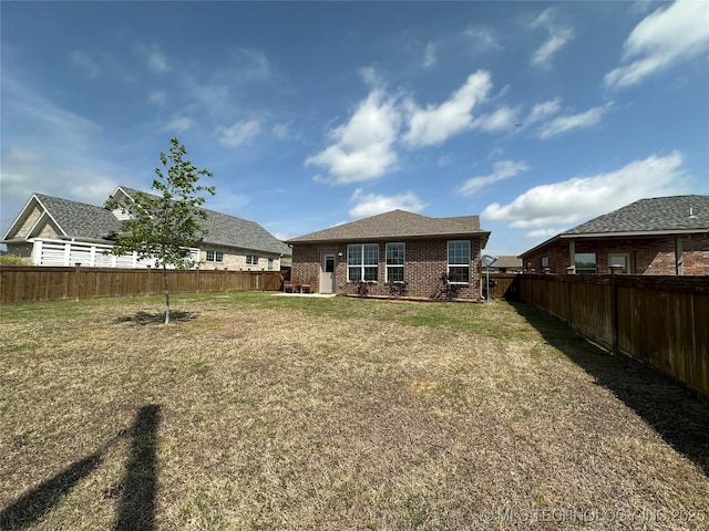 back of house featuring a fenced backyard, brick siding, and a yard