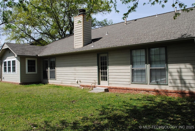 rear view of house featuring a lawn, a chimney, and a shingled roof