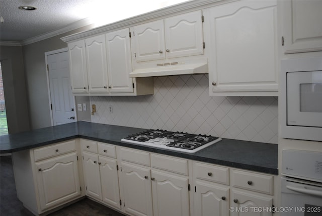 kitchen featuring backsplash, a peninsula, dark countertops, and white appliances