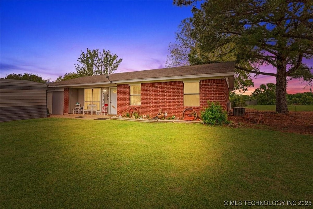 back of house at dusk with a lawn and brick siding