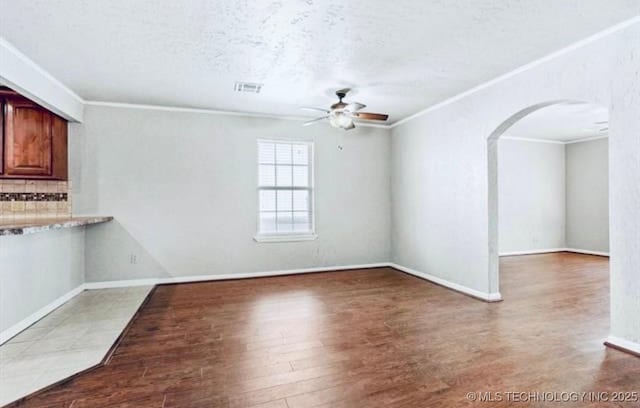 unfurnished living room featuring a ceiling fan, arched walkways, a textured ceiling, and ornamental molding