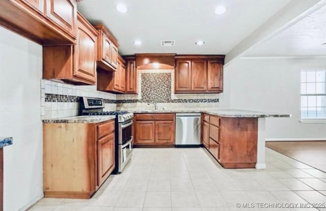 kitchen featuring a peninsula, appliances with stainless steel finishes, light stone countertops, and tasteful backsplash