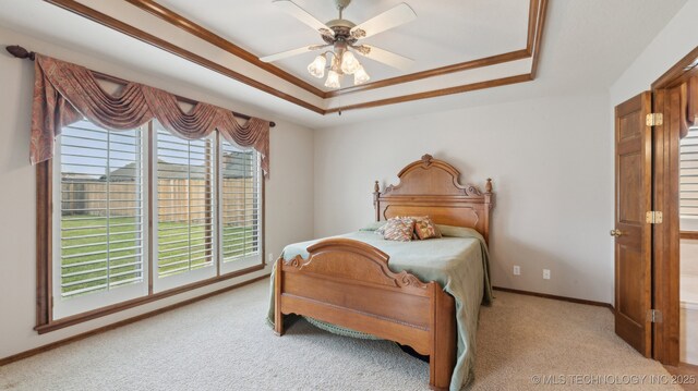bedroom with a raised ceiling, ornamental molding, baseboards, light colored carpet, and ceiling fan