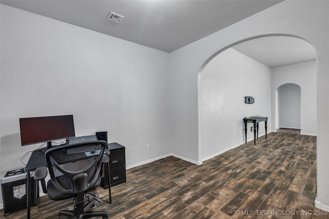 office space with arched walkways, wood finished floors, visible vents, and baseboards