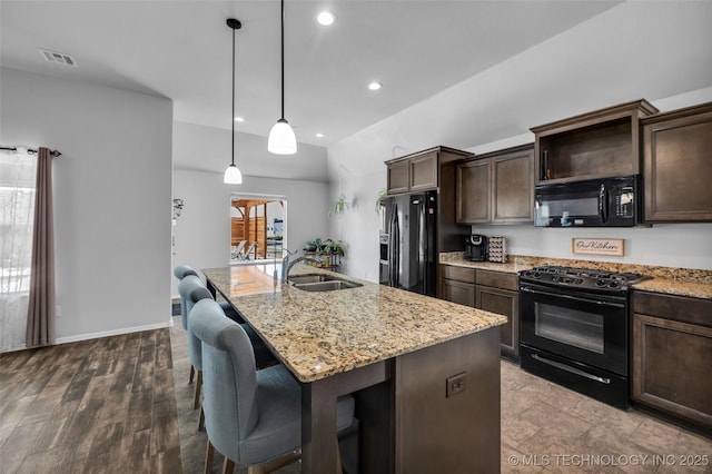 kitchen with light stone counters, a sink, black appliances, dark brown cabinetry, and a center island with sink