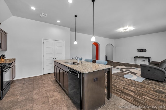 kitchen with a breakfast bar, a sink, arched walkways, dark brown cabinetry, and black appliances
