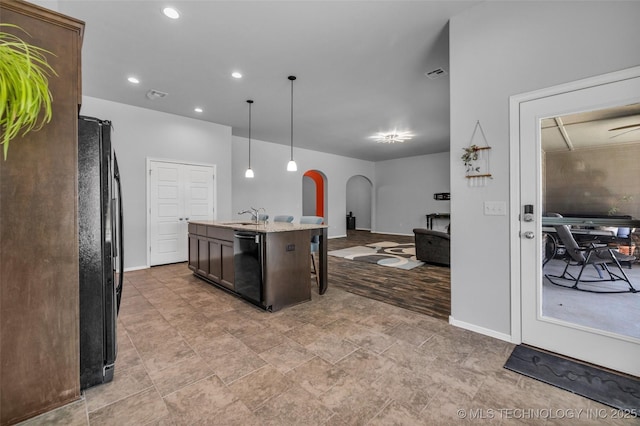 kitchen featuring dark brown cabinets, a sink, black appliances, an island with sink, and arched walkways
