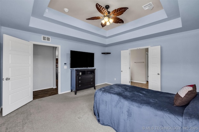 bedroom with visible vents, baseboards, a tray ceiling, and carpet