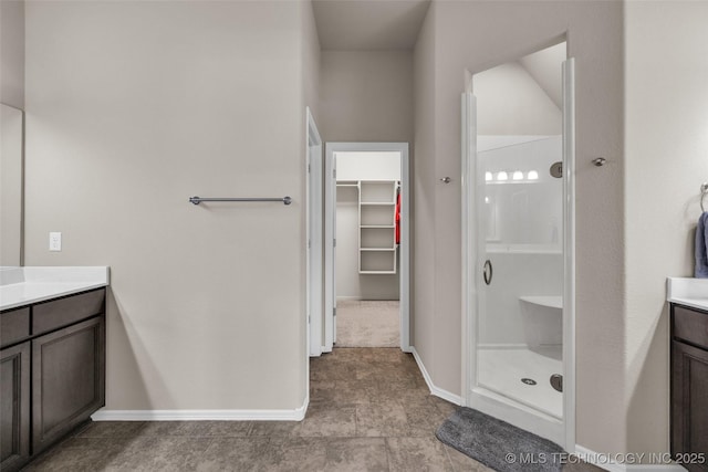bathroom featuring baseboards, vanity, a spacious closet, and a shower stall