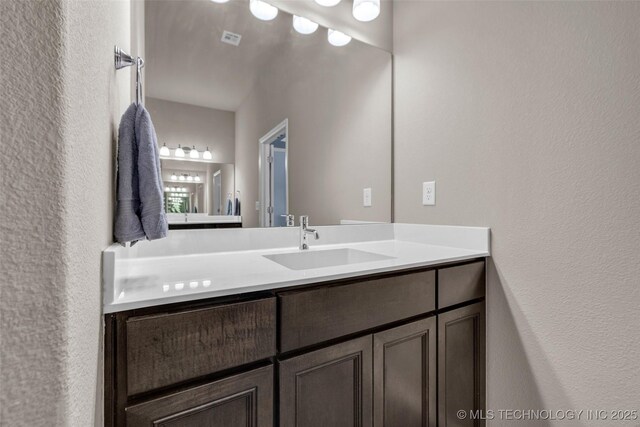 bathroom featuring a textured wall, vanity, and visible vents