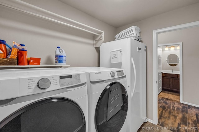 washroom with a sink, laundry area, washing machine and dryer, baseboards, and dark wood-style floors