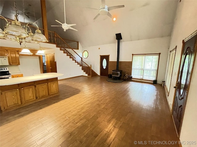 unfurnished living room with a ceiling fan, high vaulted ceiling, a wood stove, and light wood-style flooring