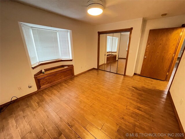 unfurnished bedroom with baseboards, wood finished floors, and a closet