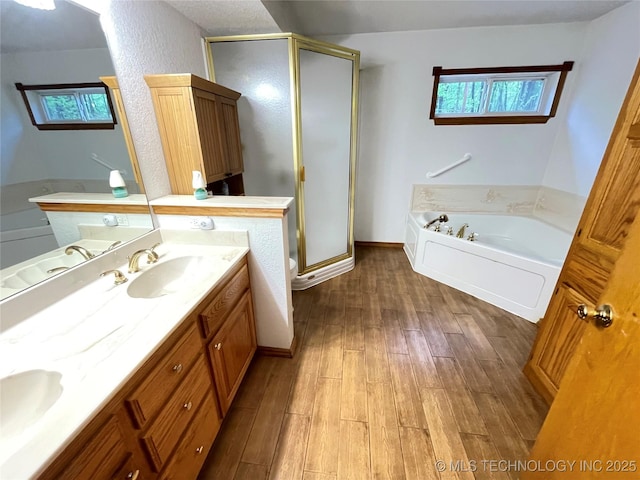 bathroom with a shower stall, double vanity, wood finished floors, a sink, and a garden tub