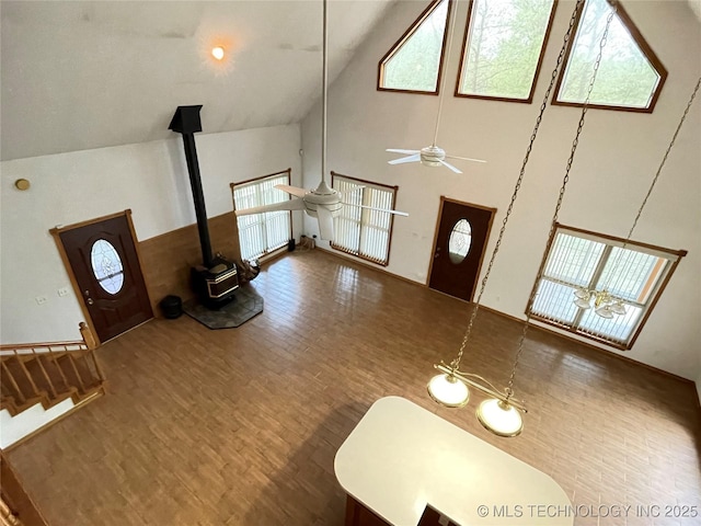 foyer entrance with wood finished floors, a wood stove, a ceiling fan, and high vaulted ceiling