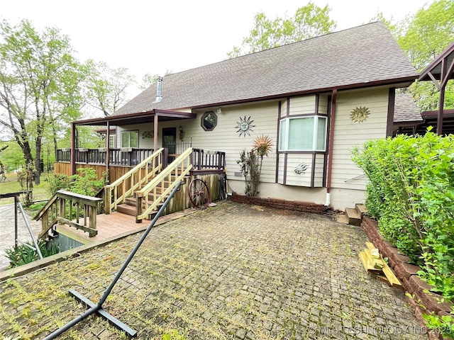view of front facade with a patio area, a shingled roof, stairway, and a deck