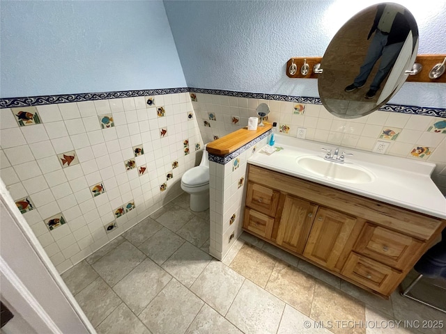 half bathroom featuring toilet, tile walls, wainscoting, a textured wall, and vanity