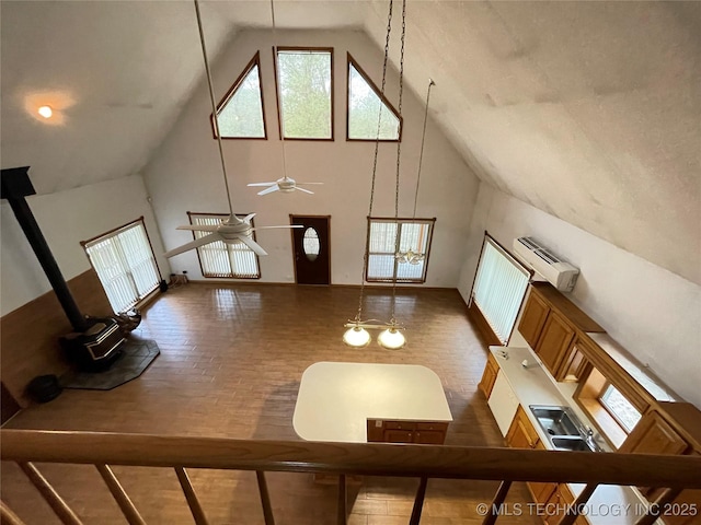 interior space with ceiling fan, a wall unit AC, high vaulted ceiling, and a wood stove