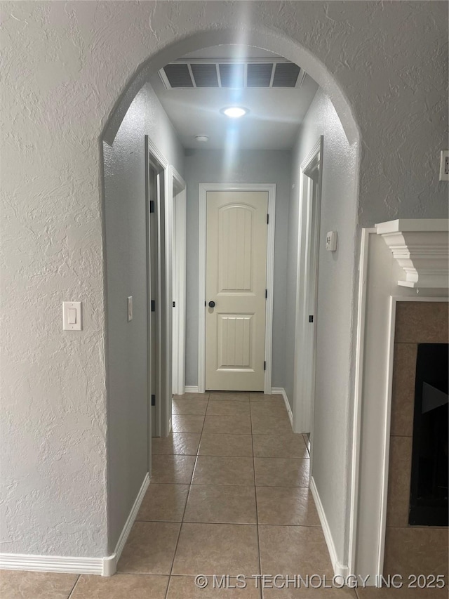 corridor featuring arched walkways, a textured wall, visible vents, and light tile patterned floors