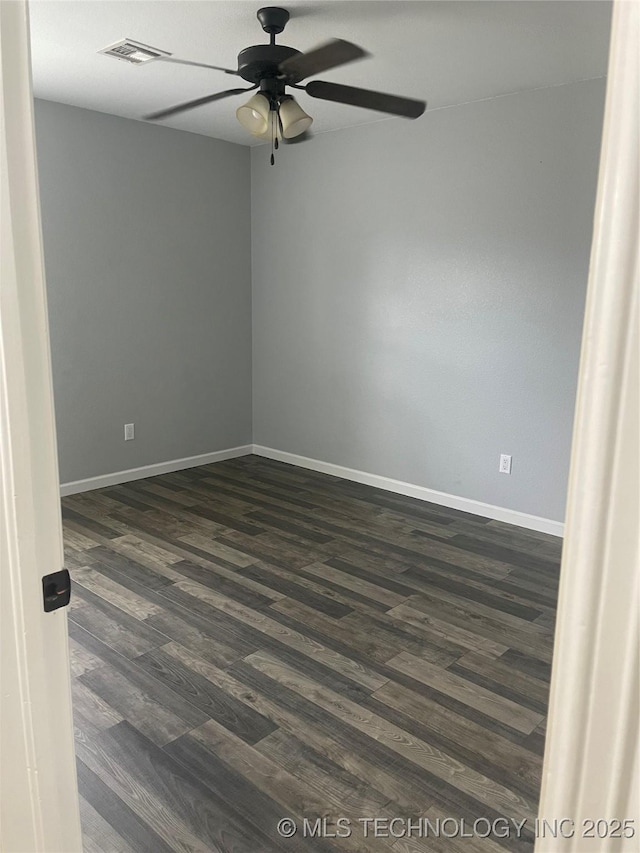 empty room with dark wood-type flooring, visible vents, a ceiling fan, and baseboards