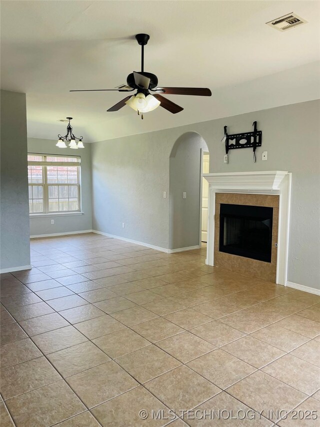 9700 E 110th St N, Owasso, OK 74055 - unfurnished living room featuring a ceiling fan, light tile patterned flooring, a tile fireplace, arched walkways, and a chandelier