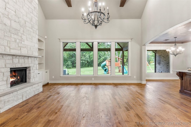 unfurnished living room with a stone fireplace, wood finished floors, high vaulted ceiling, and a notable chandelier