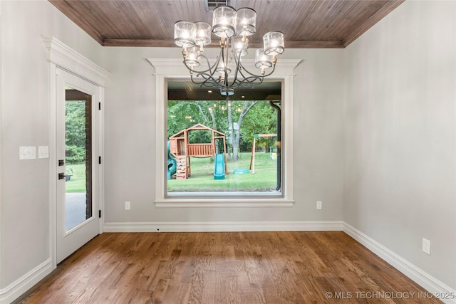 unfurnished dining area featuring wood finished floors, wooden ceiling, crown molding, baseboards, and a chandelier