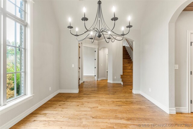 unfurnished dining area featuring arched walkways, stairs, light wood-type flooring, and plenty of natural light