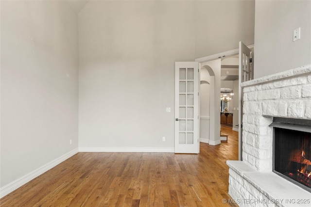 unfurnished living room with wood finished floors, a stone fireplace, a chandelier, baseboards, and a high ceiling