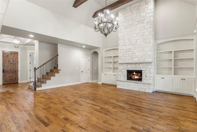 unfurnished living room featuring high vaulted ceiling, wood finished floors, a stone fireplace, an inviting chandelier, and built in features