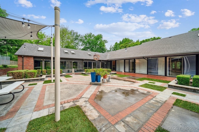 back of house featuring brick siding, a shingled roof, and a patio area