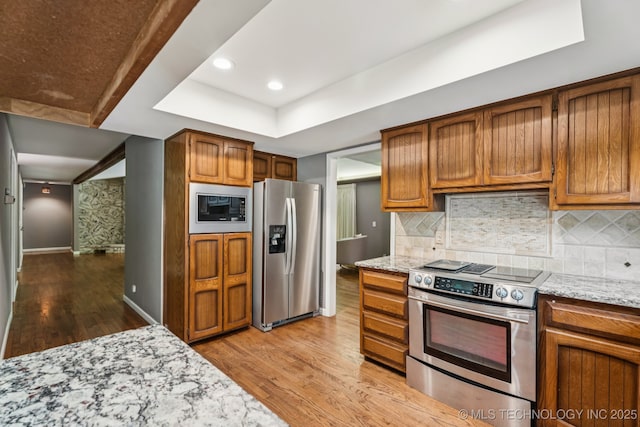 501 E Yuma Dr, Broken Arrow, OK 74011 - kitchen with appliances with stainless steel finishes, light wood-style floors, a tray ceiling, brown cabinets, and light stone counters