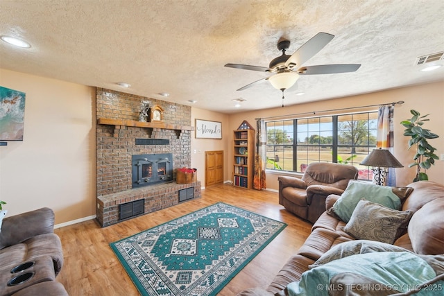 living room featuring wood finished floors, a textured ceiling, ceiling fan, a fireplace, and visible vents