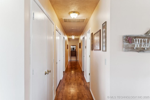 hallway featuring attic access, baseboards, wood finished floors, and visible vents