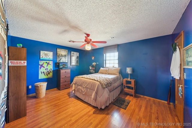 bedroom featuring wood finished floors, visible vents, a ceiling fan, baseboards, and a textured ceiling