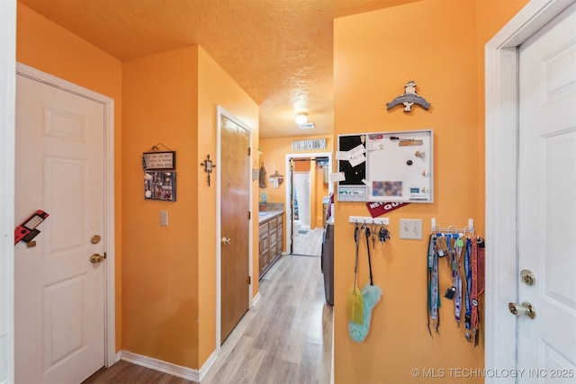 hallway with baseboards, light wood-style floors, and a textured ceiling