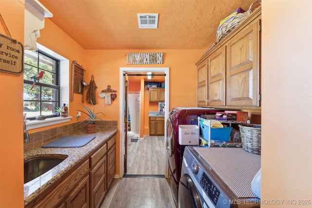 clothes washing area with washer and clothes dryer, a sink, light wood-type flooring, visible vents, and cabinet space