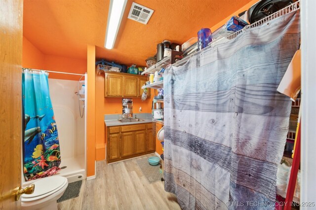 bathroom with a shower stall, wood finished floors, vanity, toilet, and visible vents