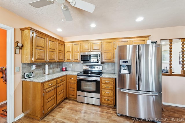 kitchen with ceiling fan, decorative backsplash, stainless steel appliances, and light wood-style floors